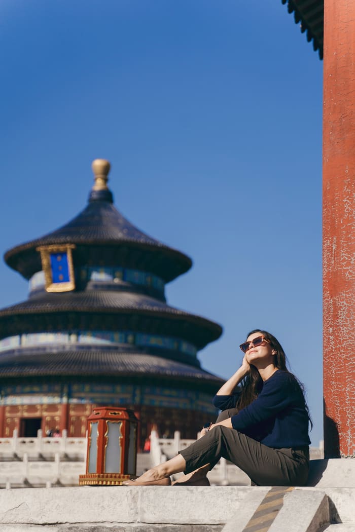mujer sentada frente a templo chino, hay un cielo azul sin nubes