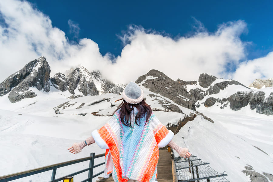 mujer de espaldas usando un gorro y un poncho en la cima de una montaña